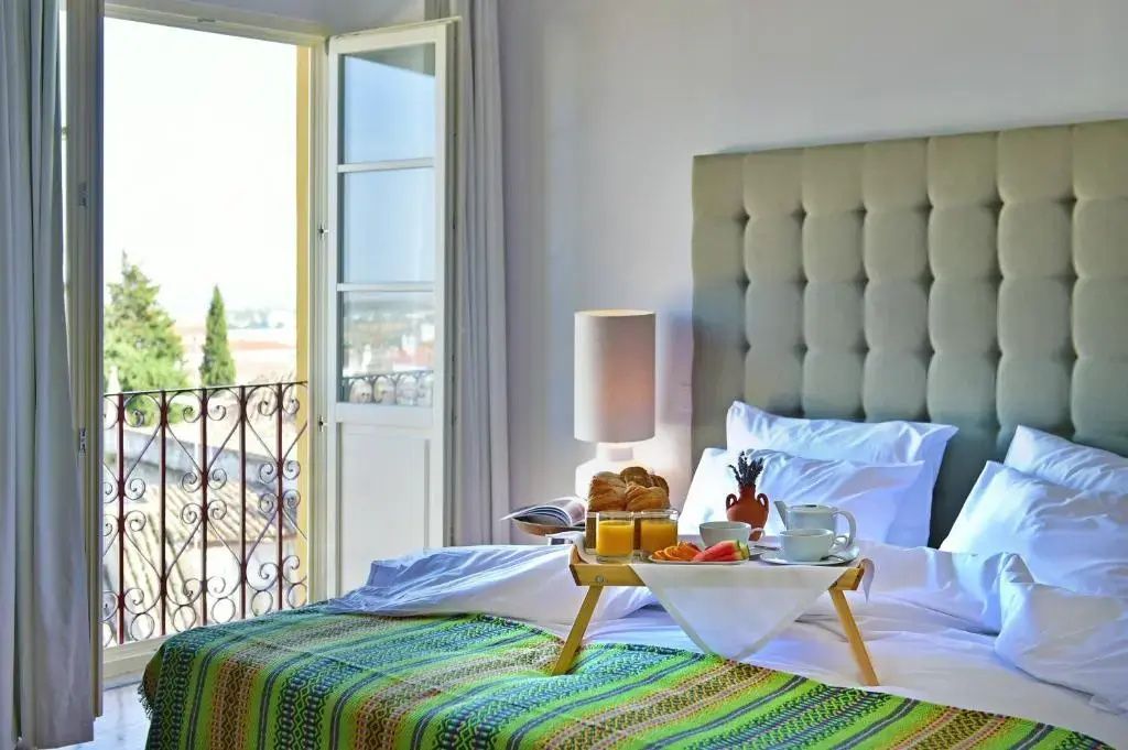 Hotelzimmer mit gemachtem Doppelbett, Frühstückstablett und Blick auf den Balkon.
