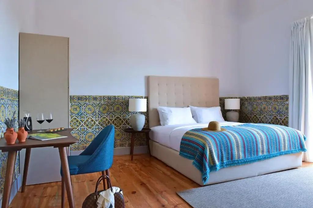 Hotelzimmer mit Doppelbett, blauem Stuhl am Schreibtisch und traditionellen Wandfliesen.