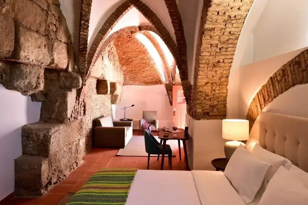Hotelzimmer mit historischem Backsteingewölbe, Steinwand, Bett und Sitzbereich mit Schreibtisch.
