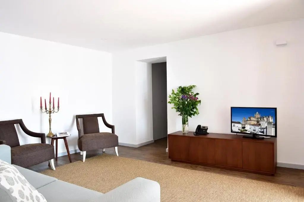 Heller Wohnbereich mit braunem Sessel, Fernseher auf einem Holzschrank und Blumen.