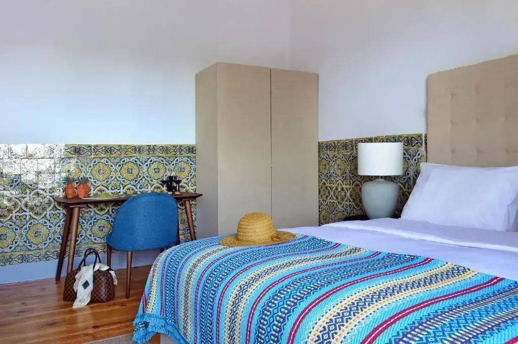 Schlafbereich im Hotelzimmer mit hellbraunem Kleiderschrank und bunt gemusterter Decke.