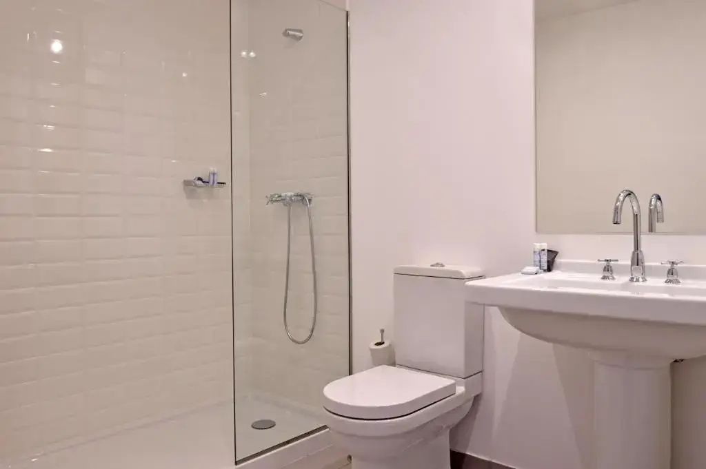 Helles Badezimmer mit ebenerdiger Glasdusche, WC und weißem Waschtisch.