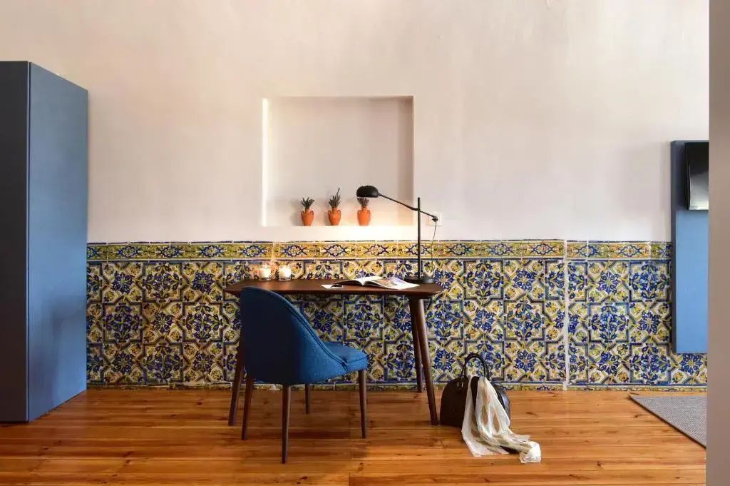 Schreibtisch aus Holz mit blauem Stuhl vor einer kunstvoll gefliesten Wand im Zimmer.
