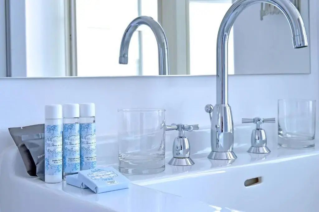 Moderner Waschtisch mit verchromtem Wasserhahn, Trinkglas und kleinen Pflegeprodukten.