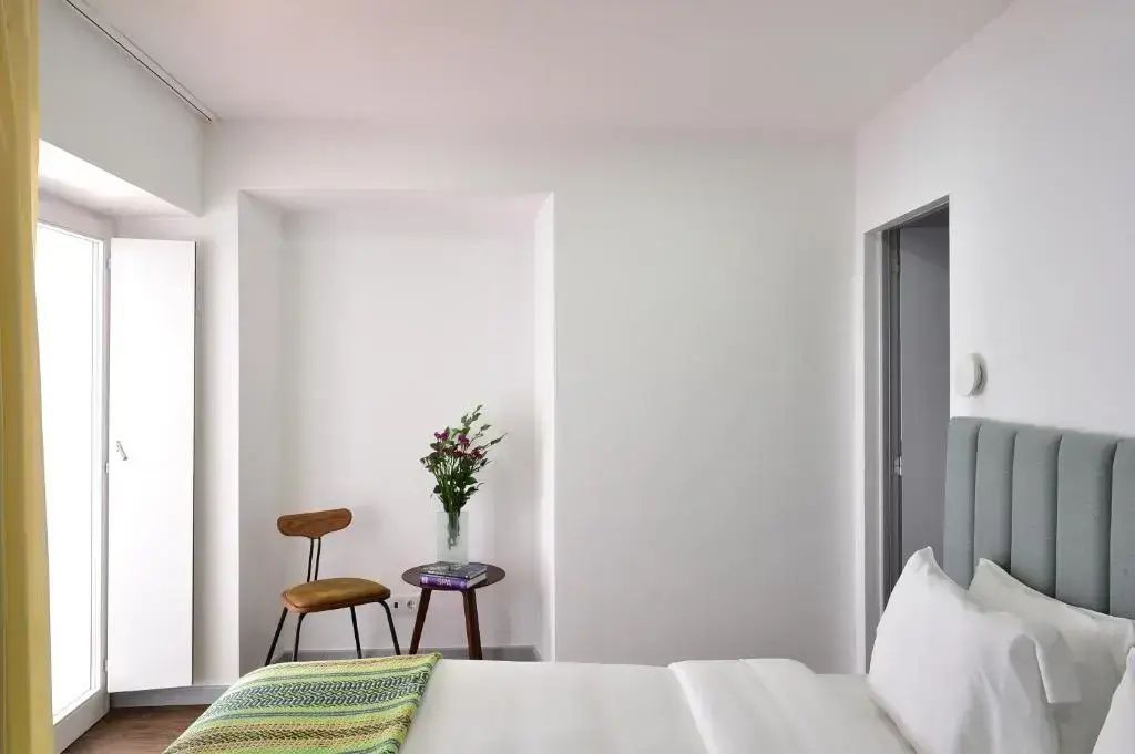 Schlafzimmer mit weiß bezogenem Bett, kleinem Beistelltisch und Holzstuhl.