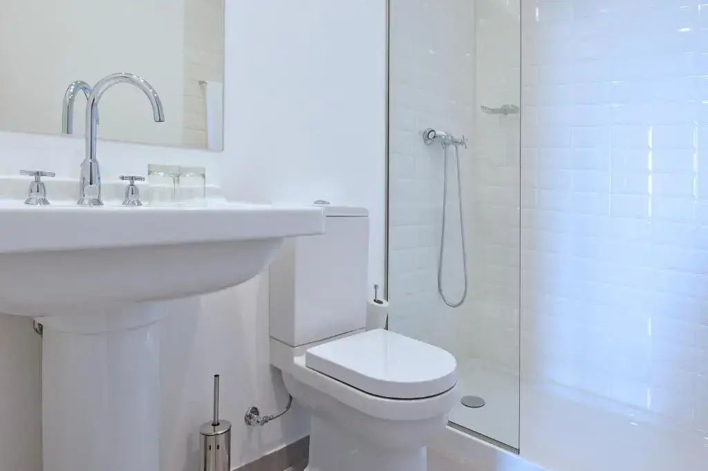 Weißes Badezimmer mit Waschtisch, Toilette und ebenerdiger Glasdusche.