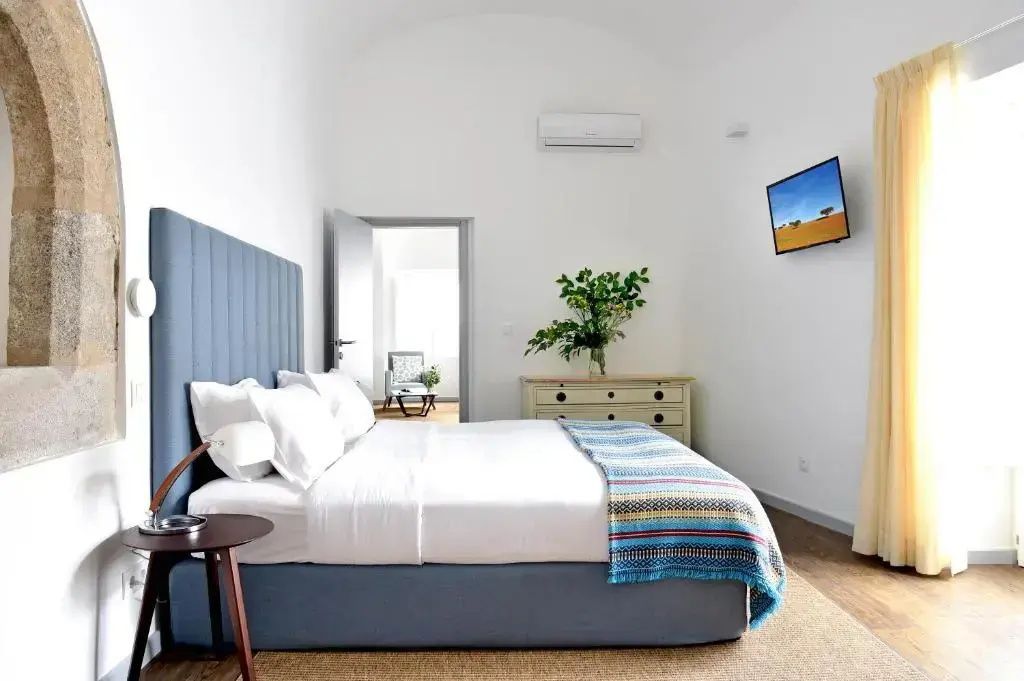 Helles Hotelzimmer mit Doppelbett, blauem Kopfteil, weißer Bettwäsche und Holzboden.