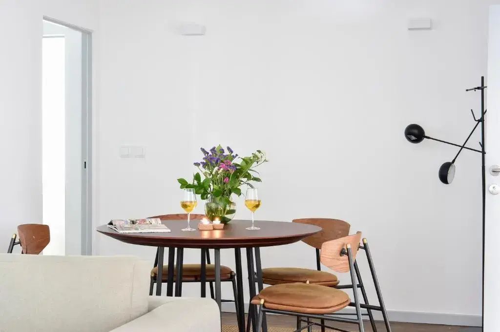 Runder Holztisch mit vier Stühlen, zwei Weingläsern und einer Blumenvase im Zimmer.