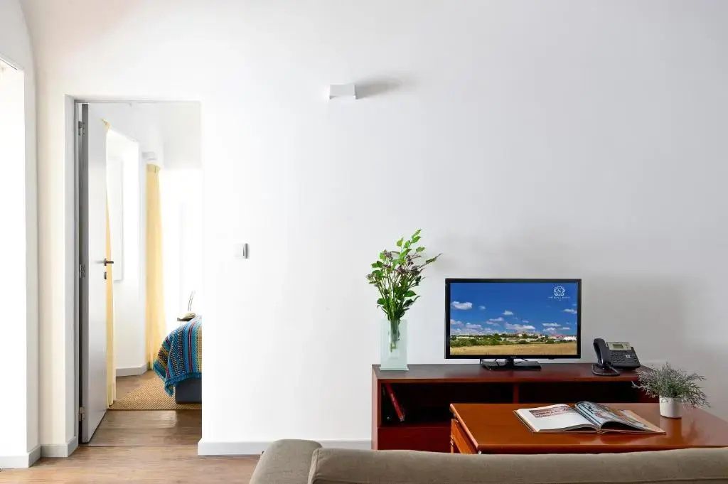 Wohnbereich mit einem Fernseher auf Holzmöbeln und Durchgang zum Schlafzimmer.