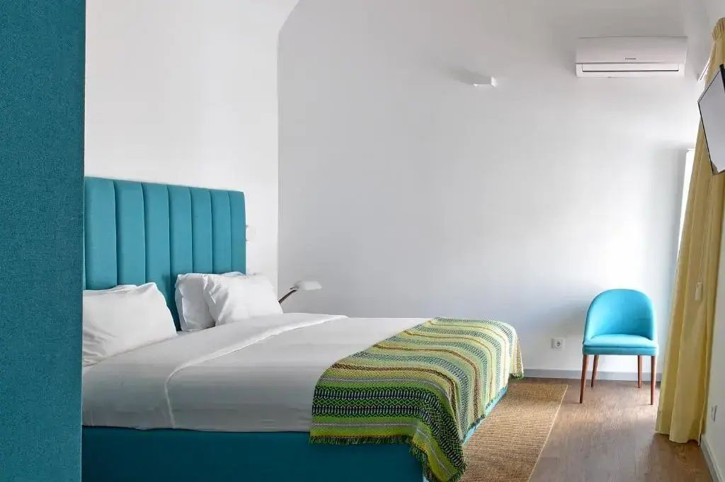 Doppelbett mit türkisblauem Kopfteil, grün gestreifter Tagesdecke und weißer Wand.