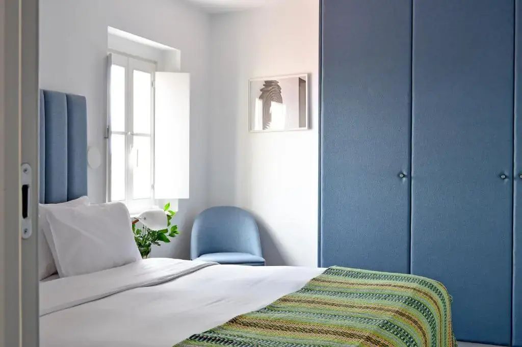 Doppelbett mit grün gemusterter Tagesdecke vor einem blauen Schrank.