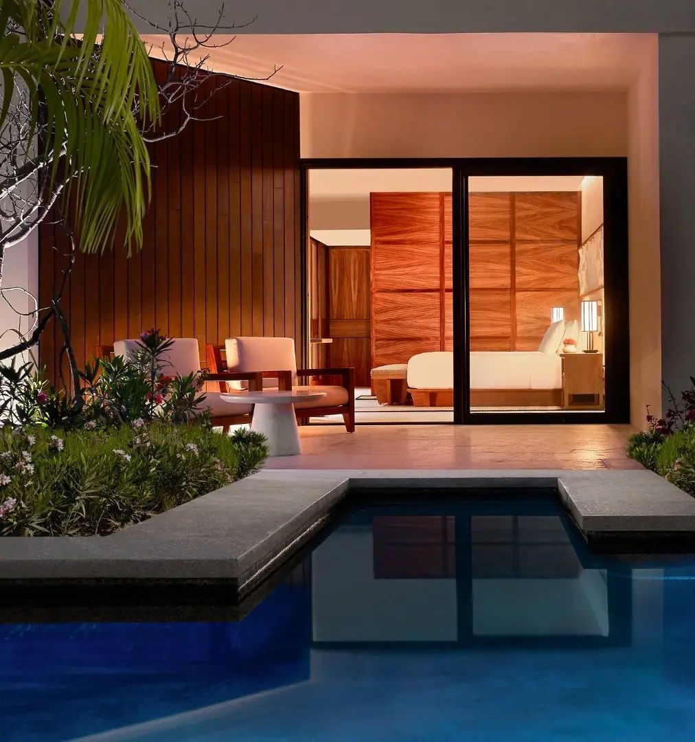 Terrasse mit eigenem kleinen Pool, Sitzgelegenheiten und Blick in das beleuchtete Zimmer.