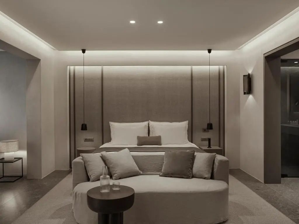 Modernes Hotelzimmer mit Doppelbett, hellem Sofa und minimalistischer Beleuchtung.