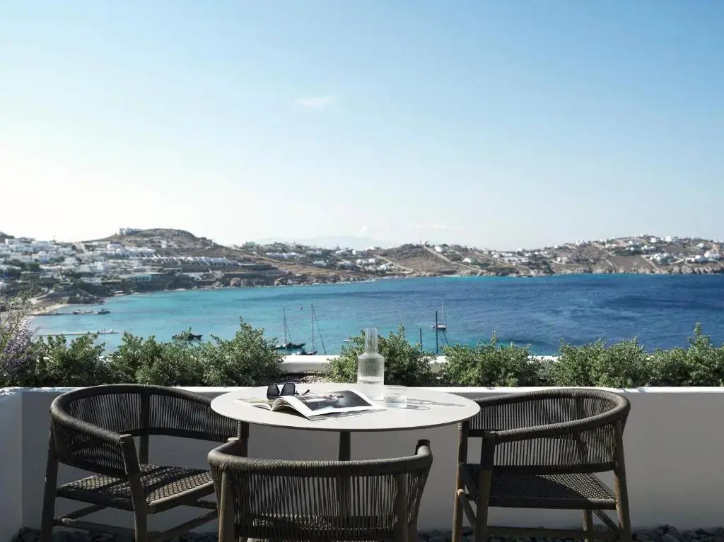 Terrasse mit Tisch und Stühlen sowie Weitblick auf eine Meeresbucht mit Booten.
