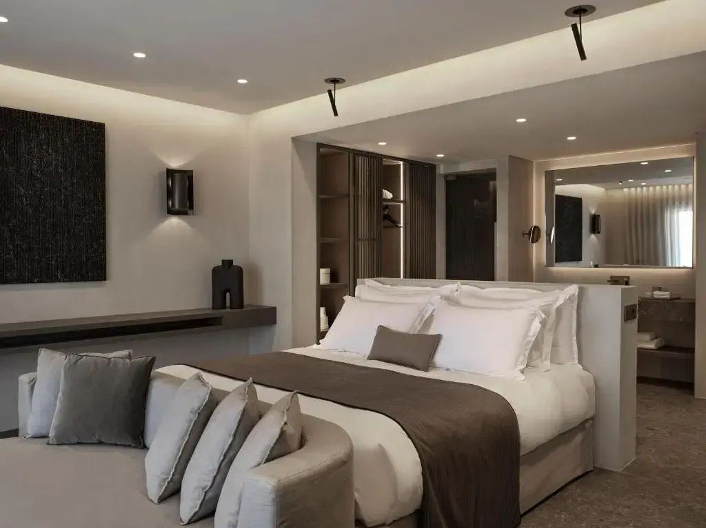 Modernes Hotelzimmer mit Doppelbett, weißer Bettwäsche und grauem Sofa.