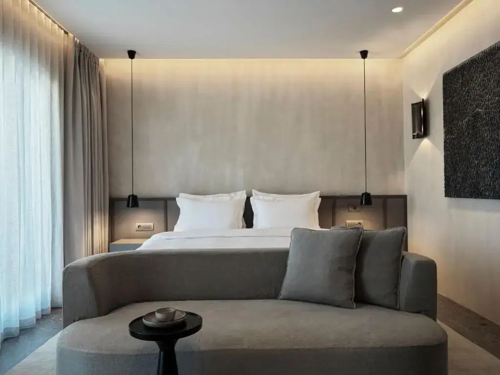 Graues Sofa vor einem Doppelbett mit zwei Pendelleuchten und indirektem Licht.
