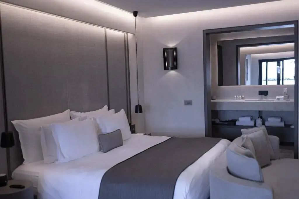 Doppelbett mit weißen Kissen und grauer Tagesdecke im Hotelzimmer.