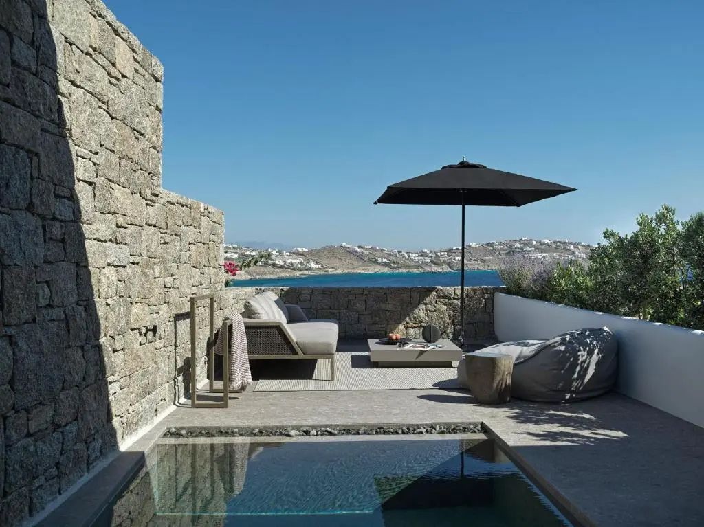 Sonnige Terrasse aus Naturstein mit Sitzbereich, dunklem Sonnenschirm und eigenem kleinem Pool.