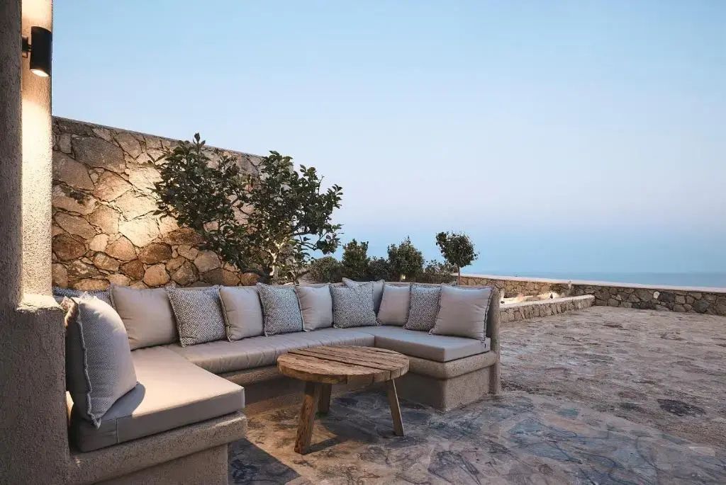 Gemauerte Terrasse mit heller Sitzgruppe, Holztisch und freiem Blick auf das Meer.