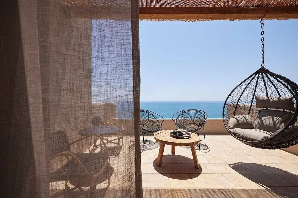 Überdachte Terrasse mit Holztisch, Stühlen, Hängesessel und unverbautem Blick auf das Meer.