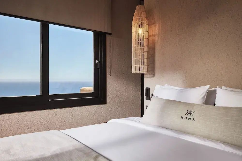 Blick durch das quadratische Fenster eines Schlafzimmers auf das blaue Meer.