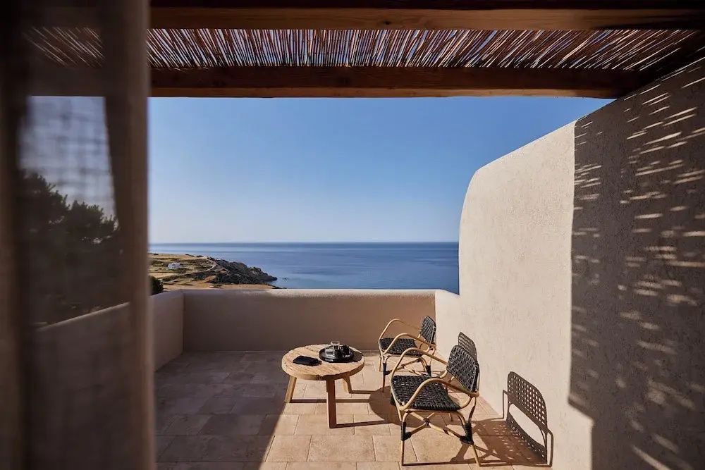 Terrasse mit Sitzgelegenheiten aus Holz und Flechtwerk mit direktem Blick auf das blaue Meer.