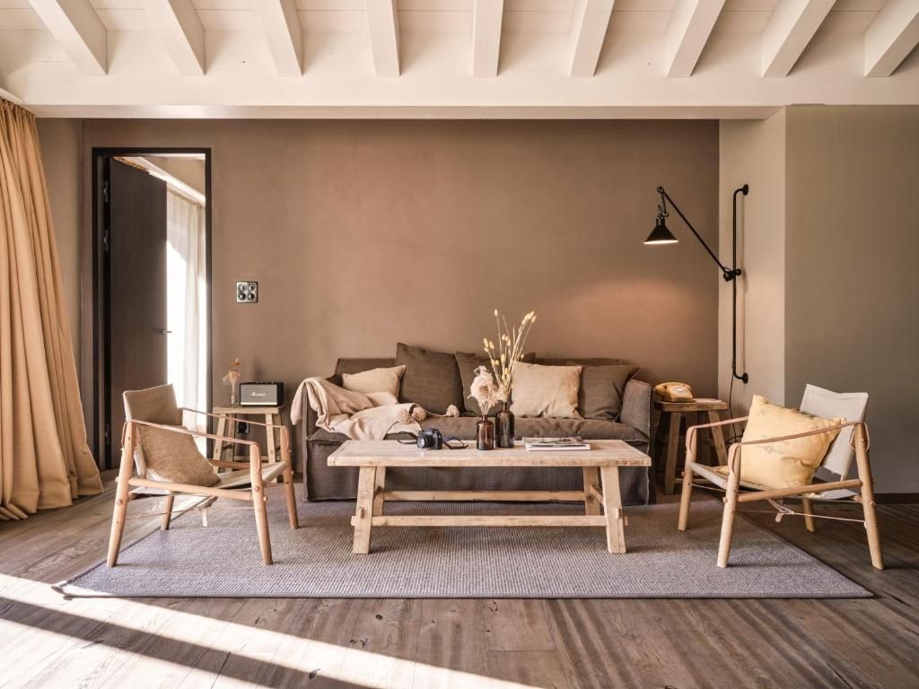 Wohnbereich mit braunem Sofa, Holztisch, zwei Sesseln und hellen Holzdeckenbalken.