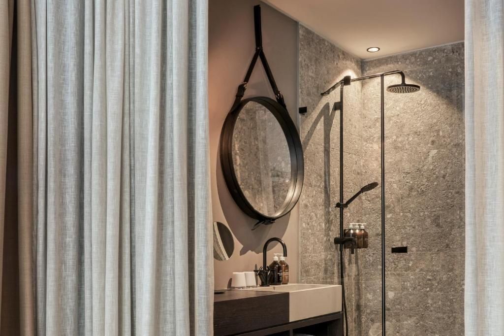 Badezimmer mit schwarzer Armatur, rundem Spiegel an Lederband und Regendusche.