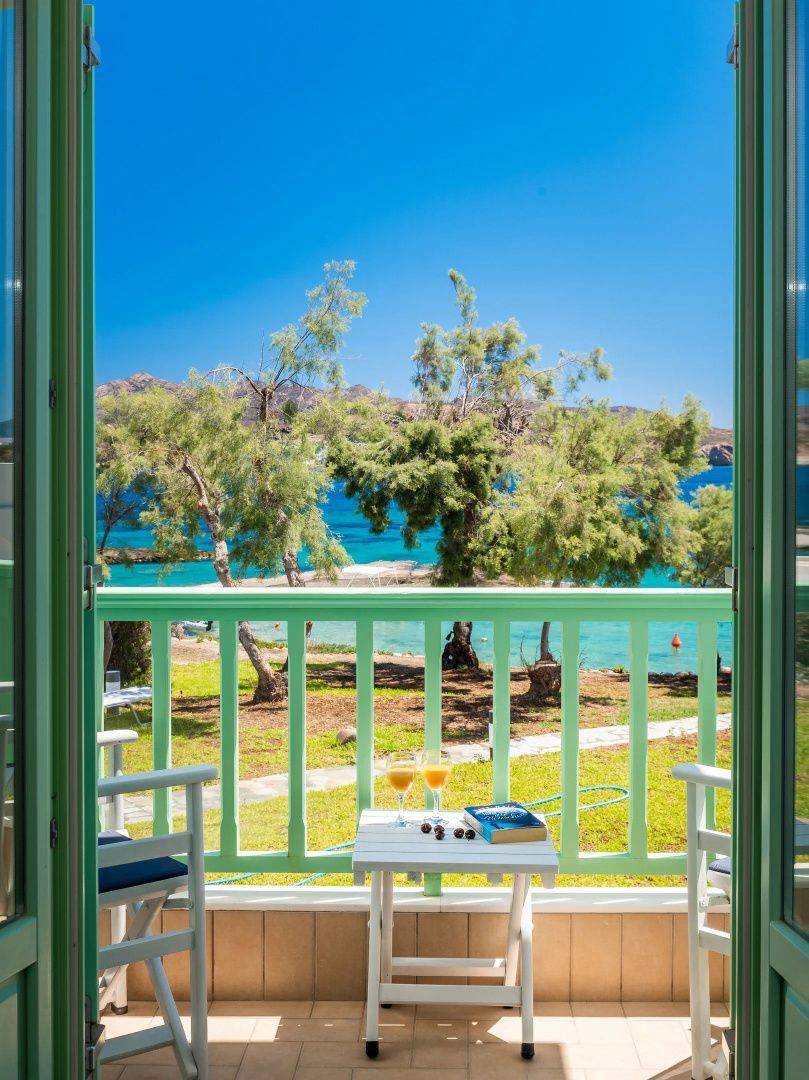 Blick von einem Balkon mit grünem Geländer auf Bäume, den Strand und das blaue Meer.