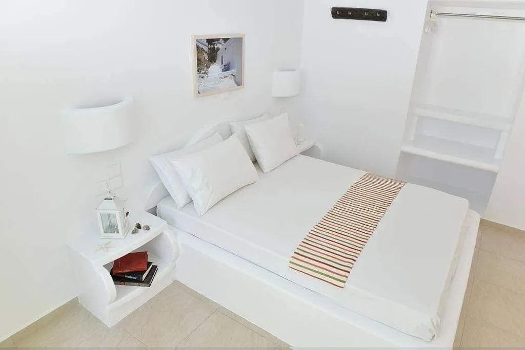 Weiß eingerichtetes Schlafzimmer mit Doppelbett, Nachttisch und Wandlampe.