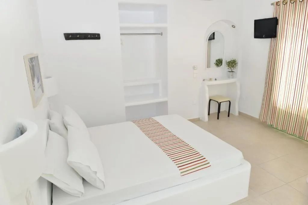 Helles Hotelzimmer in Weiß mit Doppelbett, offener Garderobe und Schminktisch.