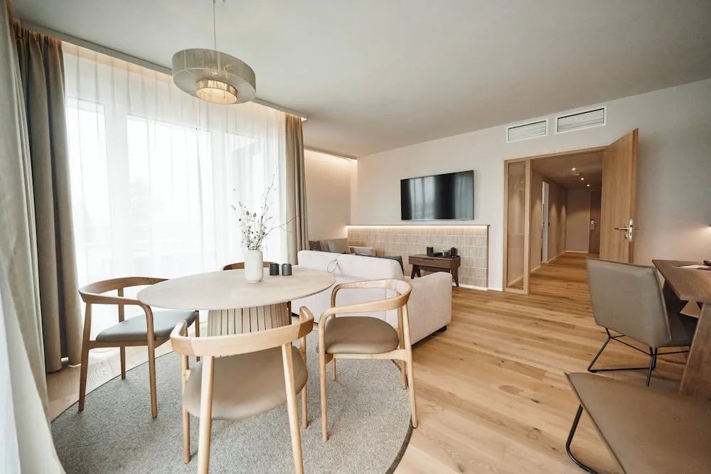 Offener Wohnbereich einer Suite mit rundem Esstisch, Sofa, TV-Gerät und hellem Holzboden.