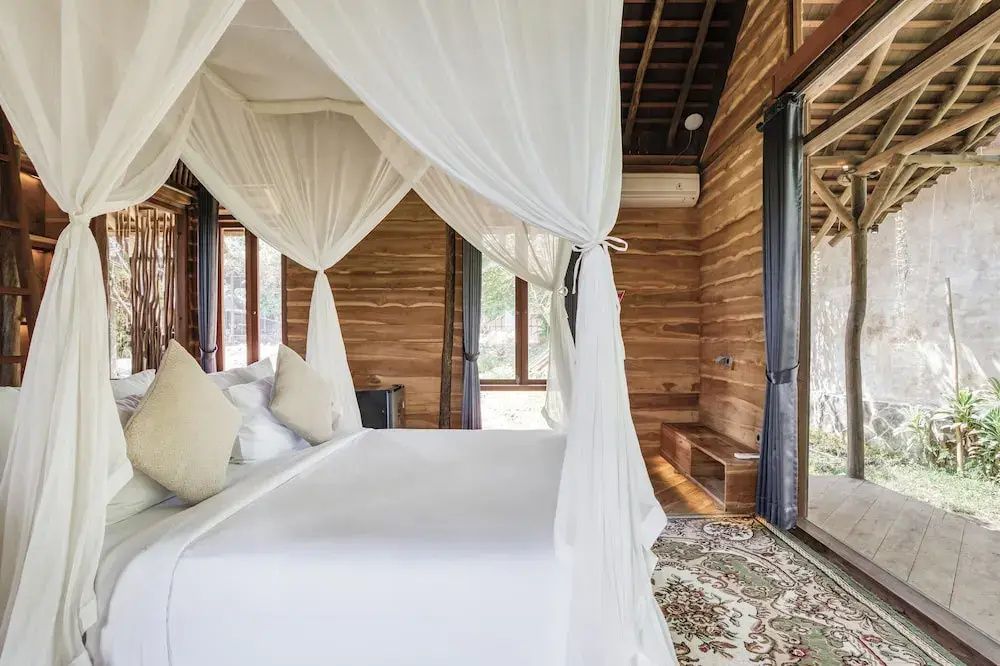 Rustikales Schlafzimmer aus Holz mit weiß verhängtem Himmelbett und großen Fenstern.