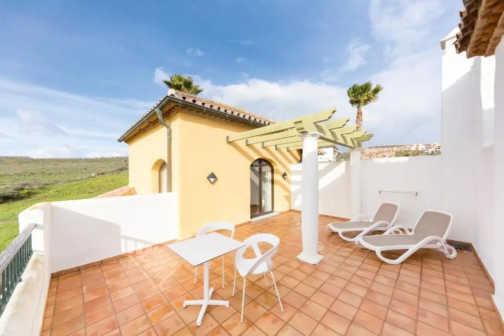 Sonnige Terrasse mit Terracottadielen, Sitzgelegenheit, Sonnenliegen und Holzpergola.