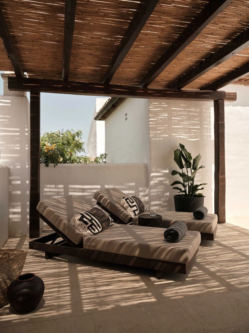 Zwei gepolsterte Sonnenliegen unter einer Pergola mit Schilfdach auf der Terrasse.
