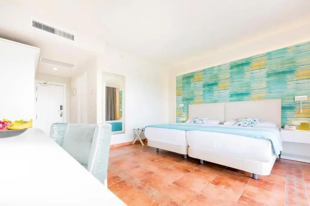 Helles Hotelzimmer mit zwei Einzelbetten, Türkistönen und Fliesenboden.