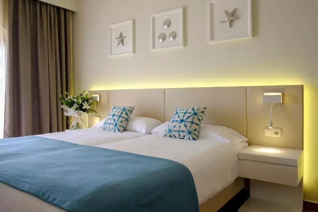 Doppelbett mit beleuchtetem Kopfteil, blauen Kissen und Bildmotive an der Wand.