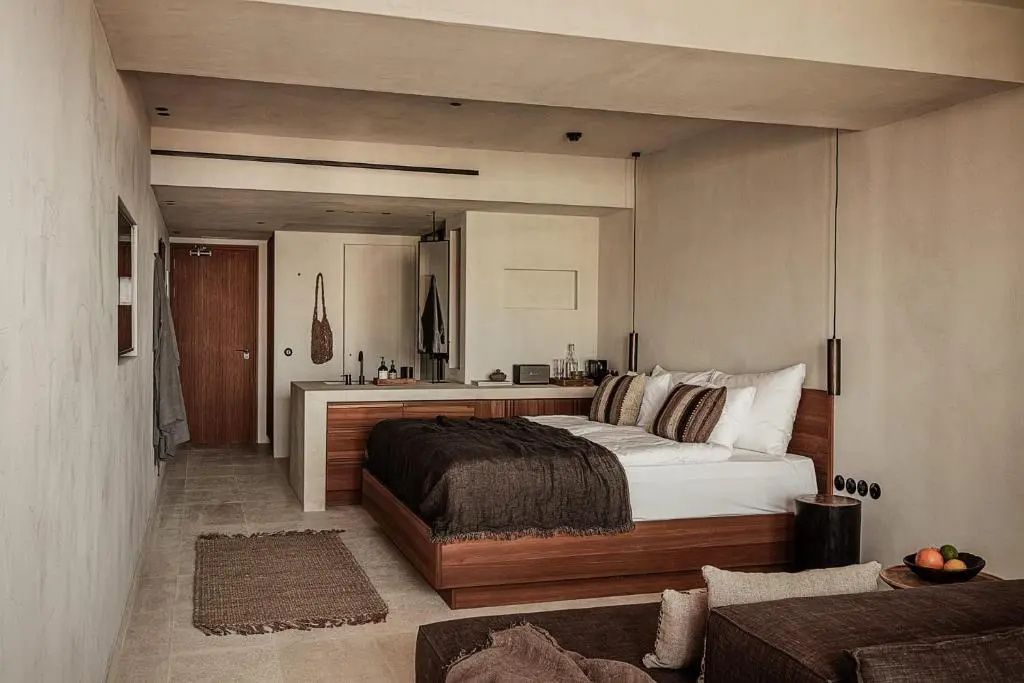 Modernes Hotelzimmer mit Holzbett, dunkelbrauner Tagesdecke und offenem Waschbereich im Hintergrund.