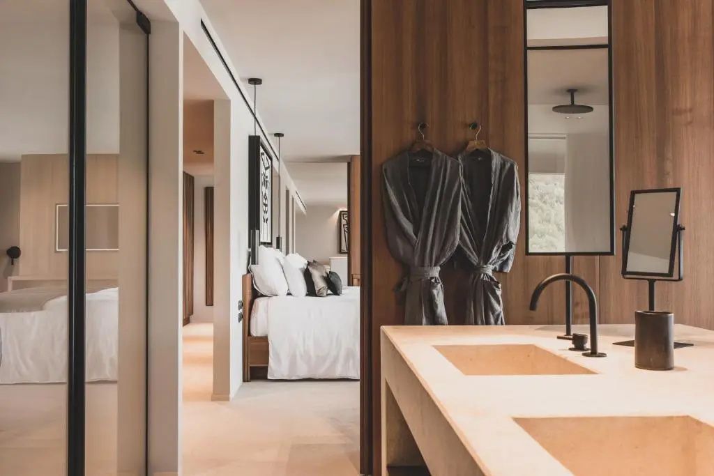 Blick aus dem offenen Badezimmer mit zwei Bademänteln auf das Doppelbett der Suite.