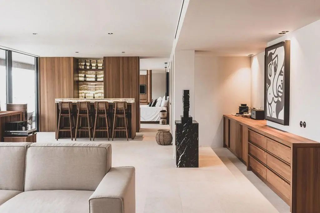 Wohnbereich einer Suite mit hellem Sofa, Holzbar und Barhockern sowie Blick zum Schlafbereich.