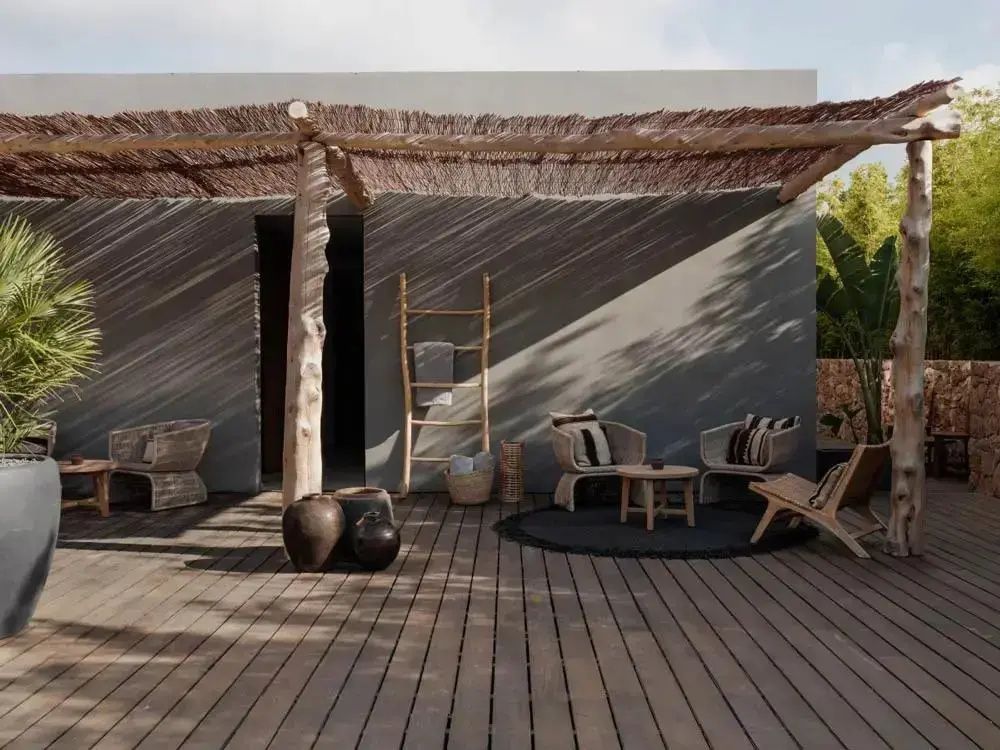 Überdachte Holzterrasse mit zwei Rattan Sesseln, einem kleinen Holztisch und Keramikvasen.