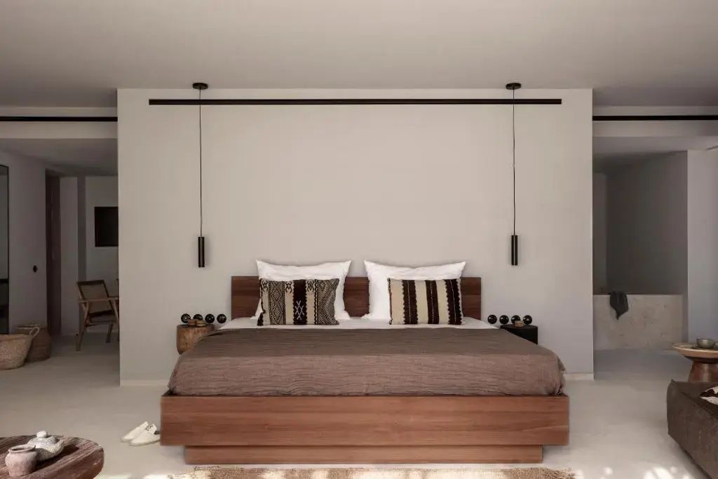Doppelbett aus Holz mit gemusterten Kissen vor einer schlichten weißen Wand.