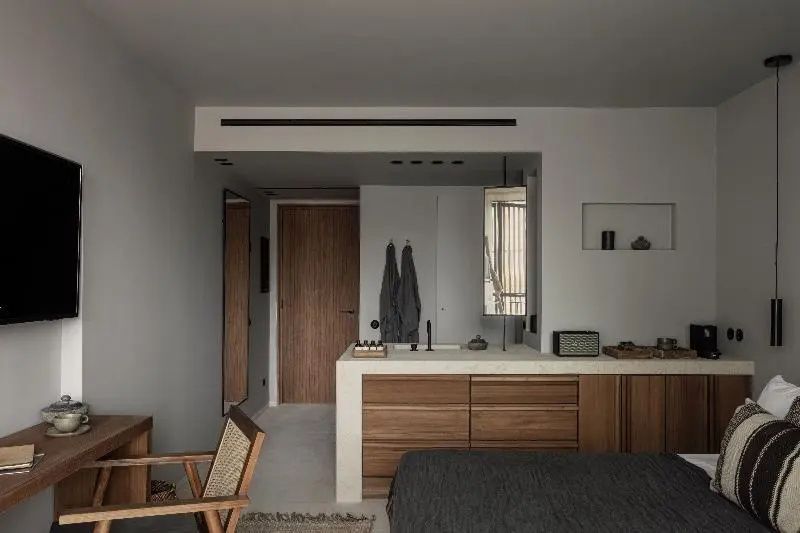 Zimmerinterieur mit Holzschränken, modernem Waschtisch und einem Flechtsessel im warmen Licht.