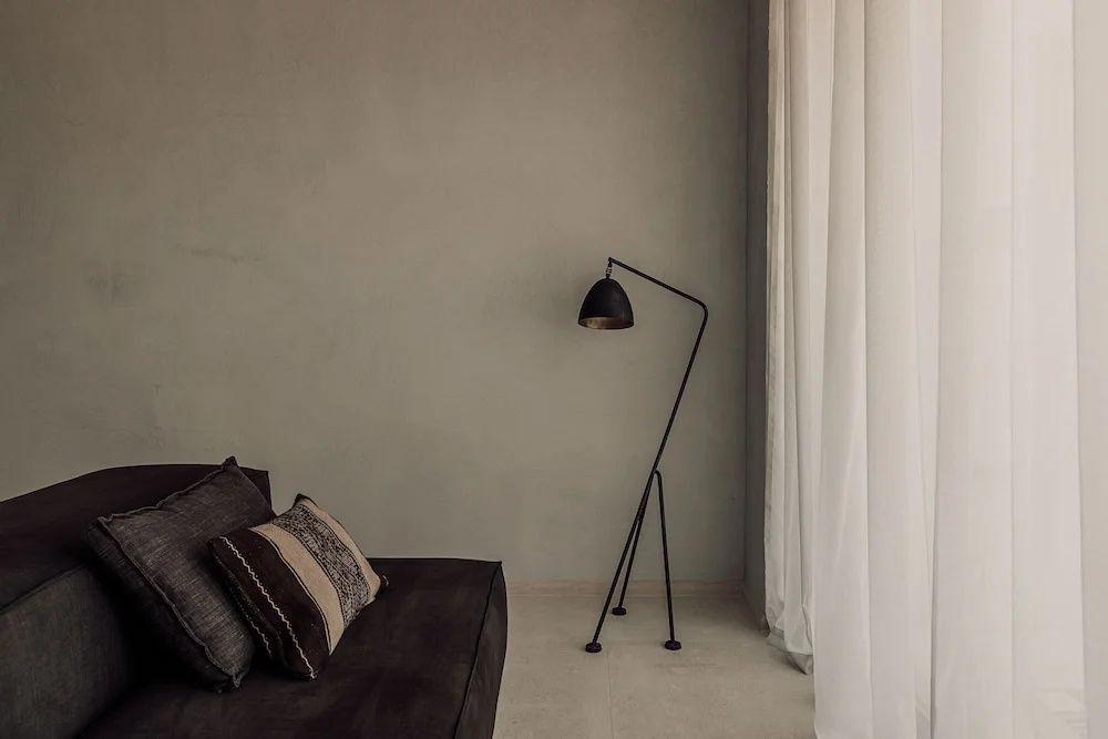 Filigrane schwarze Stehlampe in der Ecke eines Raumes neben einem dunklen Sofa mit Kissen.