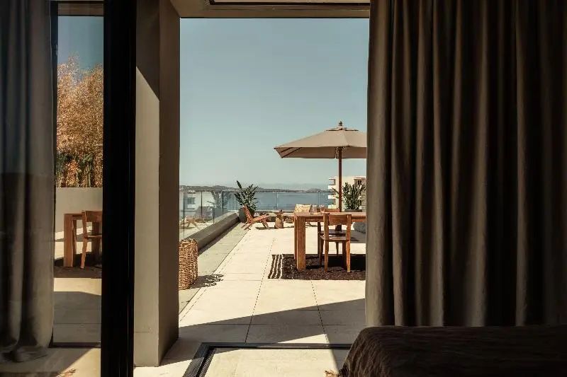 Sonnige Terrasse mit Holztisch, Sonnenschirm und Blick auf das Meer und die Küste.