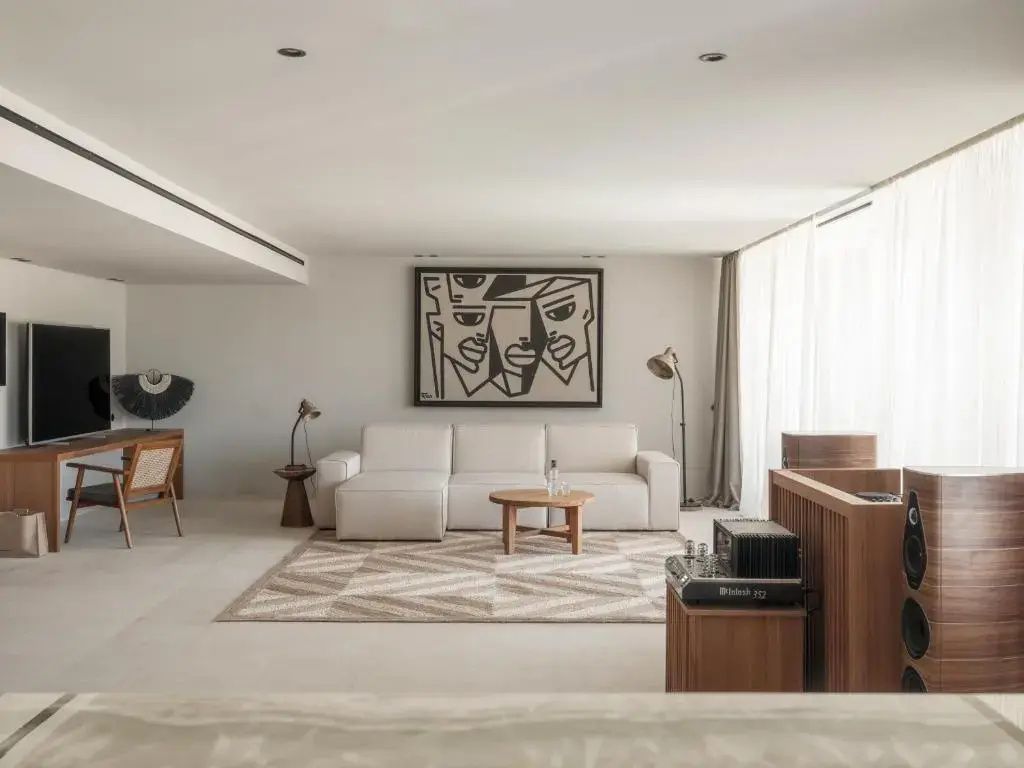 Helles Wohnzimmer mit weißer Eckcouch, Holztisch, gemustertem Teppich und Kunstwerk an der Wand.