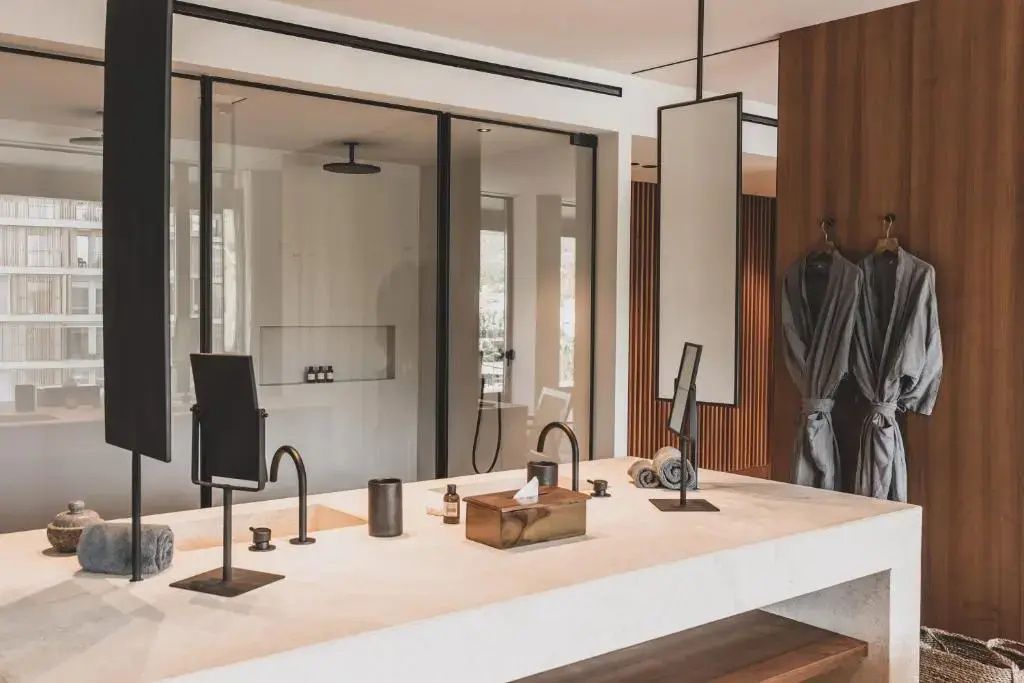 Waschtisch mit zwei Armaturen in Schwarz, Spiegeln und einer gläsernen Dusche im Hintergrund.