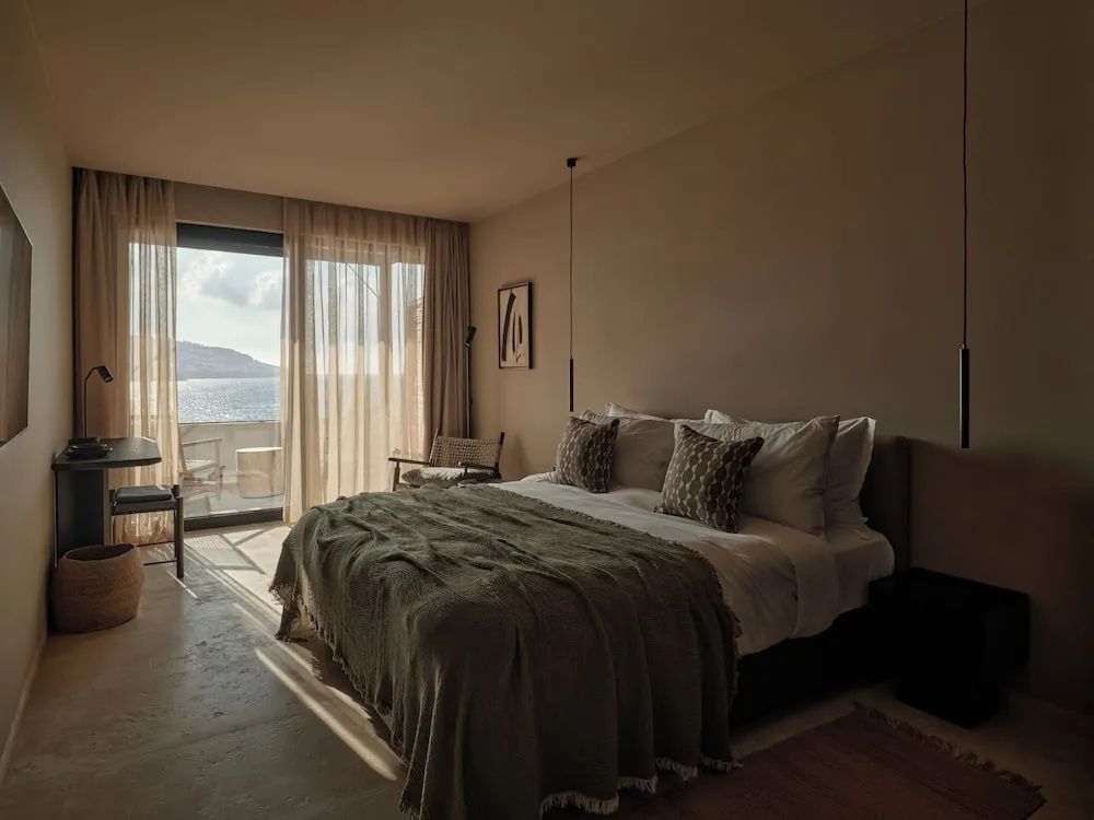 Hotelzimmer mit einem Doppelbett, leichten Vorhängen und Zugang zum Balkon mit Meerblick.