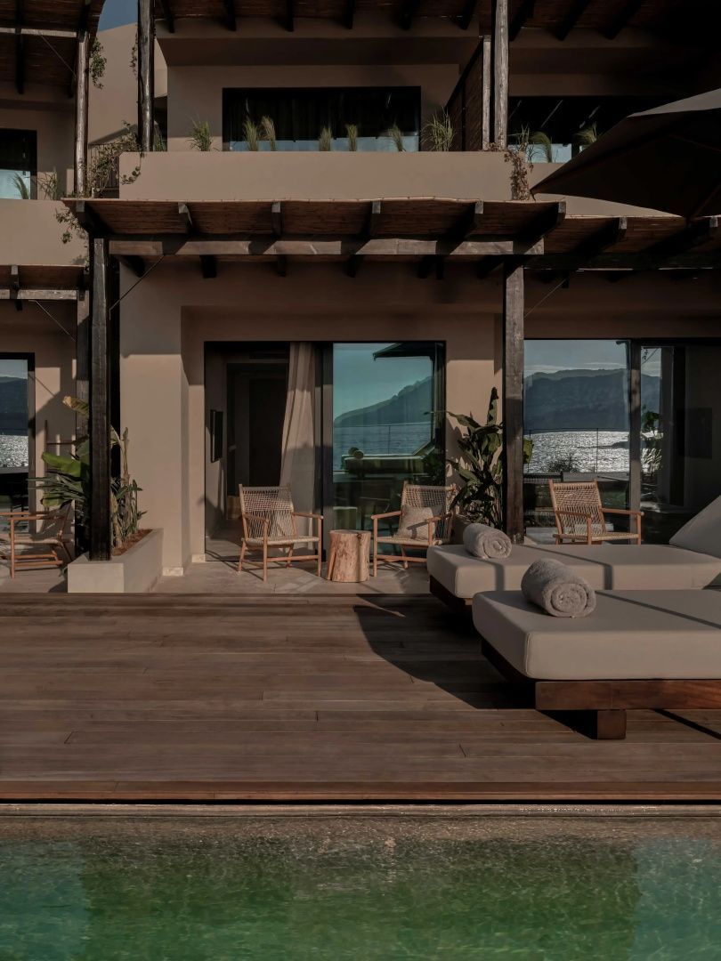 Terrasse aus Holz mit zwei Sonnensegeln, Liegestühlen und Blick auf das Meer.