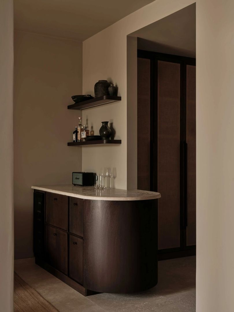 Dunkle Minibar aus Holz mit Marmorplatte und Regalen an der Wand.